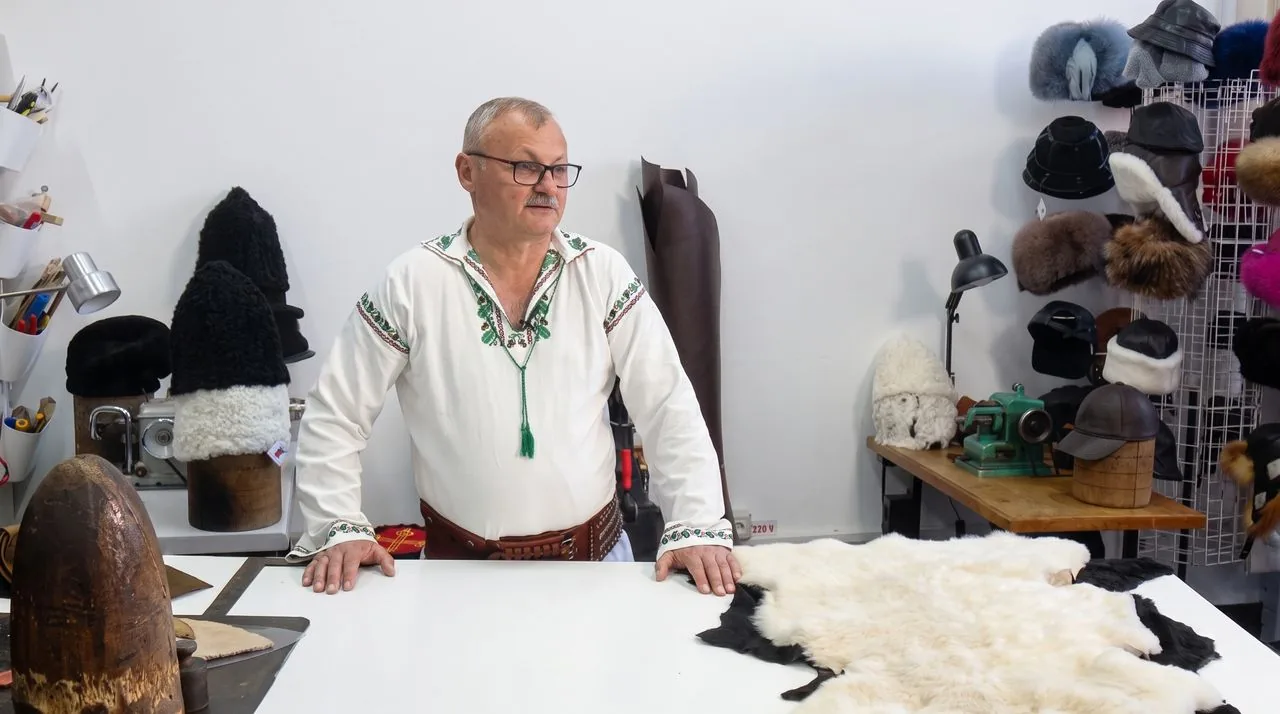 Meșterul, în picioare în spatele mesei de croit din atelier.