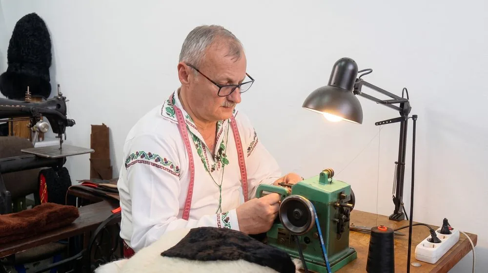 Maistrul coase o blană la mașina de blănărie verde, în atelier.